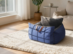 Blue pet bed with brown straps on a rug in a sunlit room